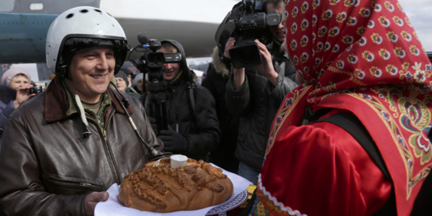 In this photo provided by the Russian Defense Ministry Press Service, a Russian pilot who returned from Syria is welcomed with traditional bread-and-salt at an airbase near the Russian city Voronezh, Tuesday, March 15, 2016. Russian warplanes and troops stationed at Russia's air base in Syria started leaving for home on Tuesday after a partial pullout order from President Vladimir Putin the previous day, a step that raises hopes for progress at the newly reconvened U.N.-brokered peace talks in