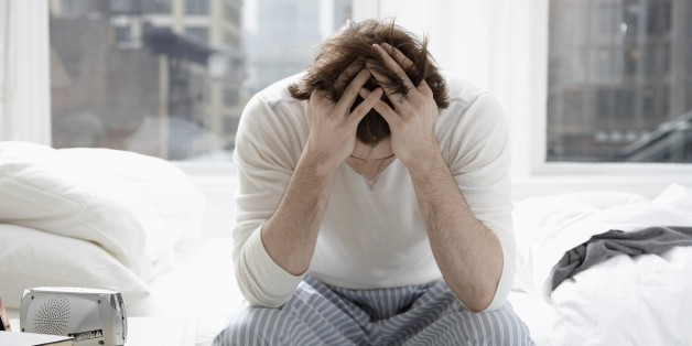 Young man sitting on bed and holding head