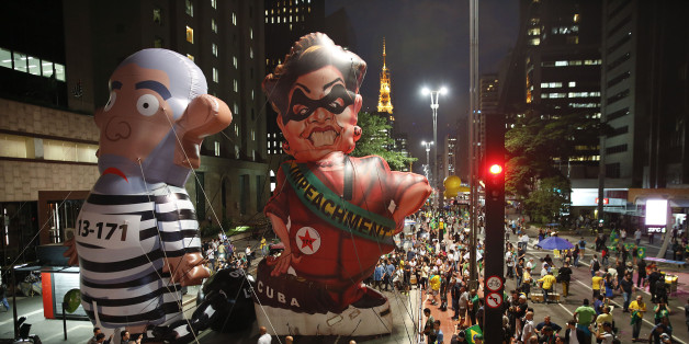 Demonstrators march alongside large, inflatable dolls depicting Brazil's former President Luiz Inacio Lula da Silva in prison garb and current President Dilma Rousseff dressed as a thief, with a presidential sash that reads "Impeachment," during a protest calling for her impeachment and against the naming of her mentor, Silva, as her new chief of staff outside the Sao Paulo's Industries Federation in Sao Paulo, Brazil, Thursday, March 17, 2016. Rousseff's critics accuse her of a transparent mane