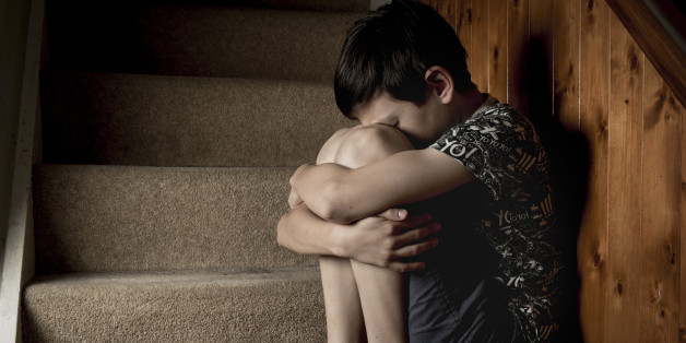 Sad, bullied or abused boy crying sitting on stairs