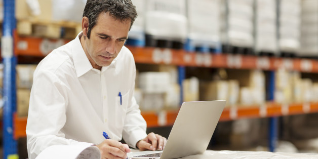 Supervisor doing paperwork while using laptop in warehouse