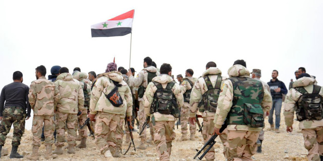 In this photo released by the Syrian official news agency SANA, Syrian soldiers gather around a Syrian national flag in Palmyra, Syria, Sunday, March 27, 2016. Syrian state media and an opposition monitoring group say government forces backed by Russian airstrikes have driven Islamic State fighters from the historic central town of Palmyra, held by the extremists since May. (SANA via AP)