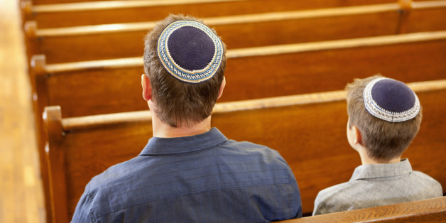 Father and son in yarmulkes sitting in synagogue