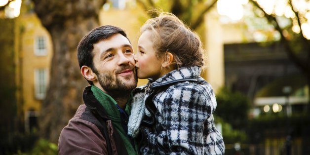 A young girl kisses her her father in an autumn park while she is kept in his arms.