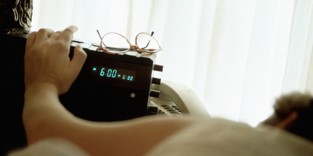 Woman in bed reaching for clock radio