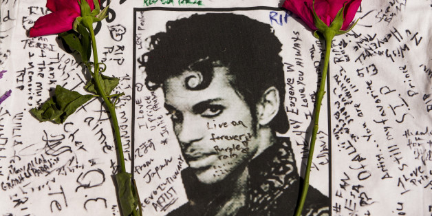Flowers lay on a T-shirt signed by fans of singer Prince at a makeshift memorial place created outside Apollo Theater in New York, Friday, April 22, 2016. The pop star died Thursday at the age of 57. (AP Photo/Andres Kudacki)