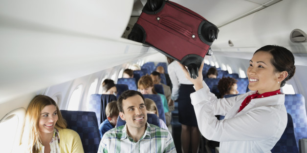 Flight attendant putting luggage in overhead bin in airplane