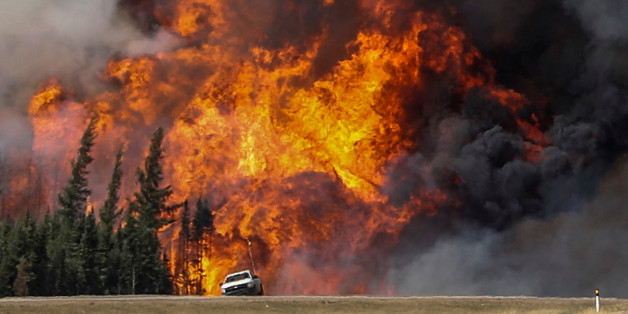 Smoke and flames from the wildfires erupt behind a car on the highway near Fort McMurray, Alberta, Canada, May 7, 2016. REUTERS/Mark Blinch TPX IMAGES OF THE DAY