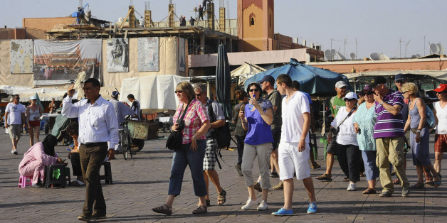 Tourists walk around the Argana restaurant (background) at Marrakesh?s famous Jemma el-Fnaa square, June 22, 2012. An Islamist bombing of a cafe last year hurt trade for the snake charmers and trinket sellers who entice foreign tourists to the Jamaa el-Fna square, but the euro zone debt crisis risks doing far more lasting damage to business. Tourists from western Europe typically account for more than 70 percent of all visitors annually to Morocco, where total visitor numbers fell 10 percent in the first quarter of 2012 from a year earlier, according to official data. Picture taken June 22, 2012. To match story MOROCCO-ECONOMY/TOURISM. REUTERS/Abderrahmane Mokhtari (MOROCCO - Tags: TRAVEL SOCIETY BUSINESS)