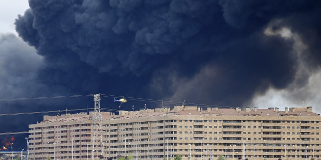 A fire fighting helicopter flies billowing black smoke rising from behind large housing blocks in Sesena, central Spain, Friday, May 13, 2016. A massive fire is raging at a sprawling tire dump in a town near Madrid, sending a spectacular cloud of thick black smoke into the air that's visible for at least 30 kilometers (20 miles). Ten teams of firefighters are trying to put out the blaze at the tire dump in the town of Sesena, still raging more than 10 hours after it started. (AP Photo/Paul White)