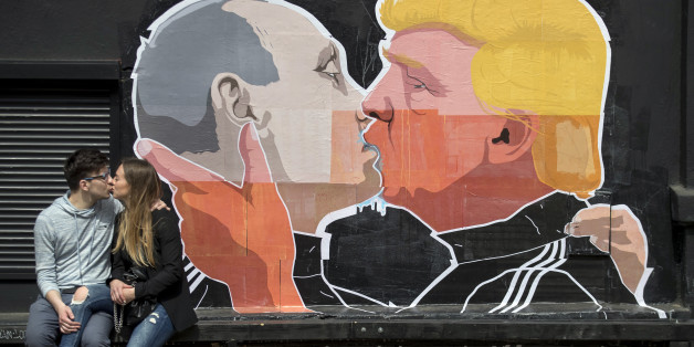 A couple kisses in front of graffiti depicting Russian President Vladimir Putin, left, and Republican presidential candidate Donald Trump, on the walls of a bar in the old town in Vilnius, Lithuania, Saturday, May 14, 2016. (AP Photo/Mindaugas Kulbis)