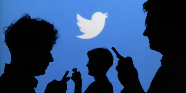 People holding mobile phones are silhouetted against a backdrop projected with the Twitter logo in this illustration picture taken in Warsaw September 27, 2013. Twitter Inc, the eight-year-old online messaging service, gave potential investors their first glance at its financials on Thursday when it publicly filed its IPO documents, setting the stage for one of the most-anticipated debuts in over a year. Picture taken September 27. REUTERS/Kacper Pempel (POLAND - Tags: BUSINESS TELECOMS LOGO)