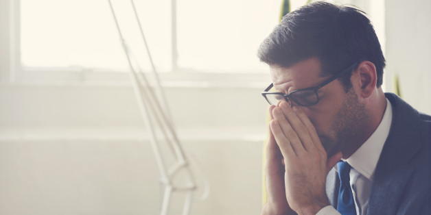 Businessman looking stressed. He is wearing a suit and glasses and holding his head in his hands. He could also have a headache