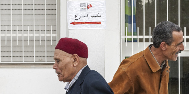 Tunisians walk past a polling station in Tunis, Tunisia, Sunday Dec. 21 , 2014. Tunisians voted on Sunday for a new president in a runoff between a symbol of the country's previous regimes and a veteran human rights activist who came to power after the revolution of 2011. (AP Photo/Ilyess Osmane)