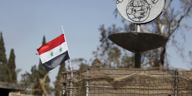 A Syrian national flag flutters next to the Islamic State's slogan at a roundabout where executions were carried out by ISIS militants in the city of Palmyra, in Homs Governorate, Syria in this April 1, 2016 file photo. To match MIDEAST-CRISIS/SYRIA- INSIGHT REUTERS/Omar Sanadiki/Files