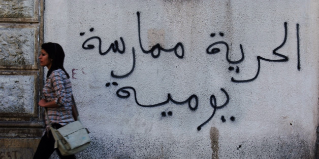 A Tunisian woman walks past a graffiti which reads, "Freedom is a daily practice" in Tunis April 26, 2011. Tunisia has boasted some of the most advanced women's rights in the Arab world. But Tunisian women are now carefully watching to see whether the uprising that ousted authoritarian President Zine al-Abidine Ben Ali on Jan. 14 will also unravel women's rights bolstered by his secular regime in a predominantly Muslim country. Picture taken April 26, 2011. To match Feature TUNISIA-WOMEN/ REUTERS/Anis Mili (TUNISIA - Tags: POLITICS CIVIL UNREST SOCIETY)