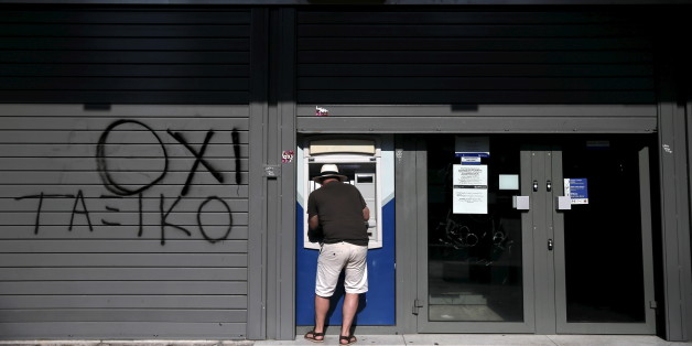 A tourist uses an ATM at a closed Attica Bank branch in Athens, Greece July 13, 2015. Euro zone leaders clinched a deal with Greece on Monday to negotiate a third bailout to keep the near-bankrupt country in the euro zone after a whole night of haggling at an emergency summit. The graffiti reads, " A 'No' of the classes". REUTERS/Alkis Konstantinidis