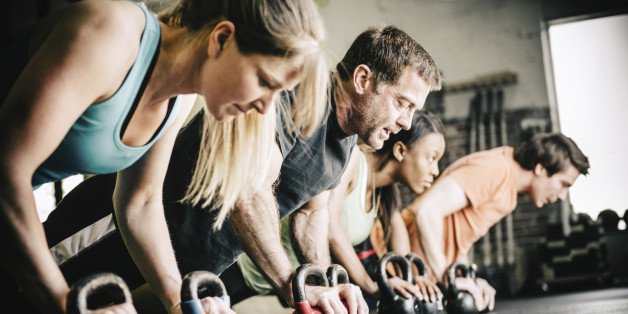 gym personal trainer doing push ups on kettle bells with small group of people in Gym.