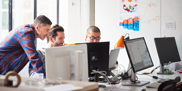Three happy businessmen working together on a computer in a tech start-up office