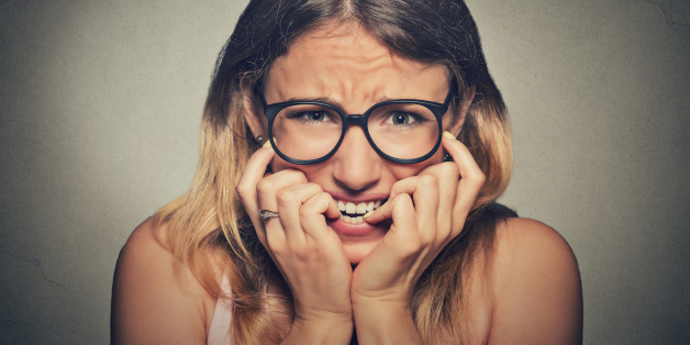 Closeup portrait nervous stressed young woman girl in glasses student biting fingernails looking anxiously craving something isolated on grey wall background. Human emotion face expression feeling