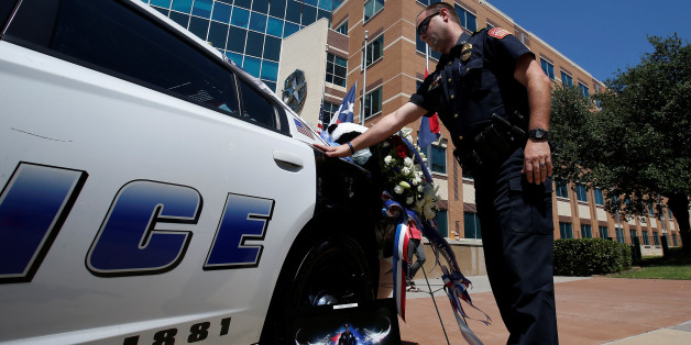 An officer touches a police car during a personal moment of silence at a makeshift memorial at Police Headquarters following the multiple police shooting in Dallas, Texas, U.S.,July 8, 2016. REUTERS/Carlo Allegri