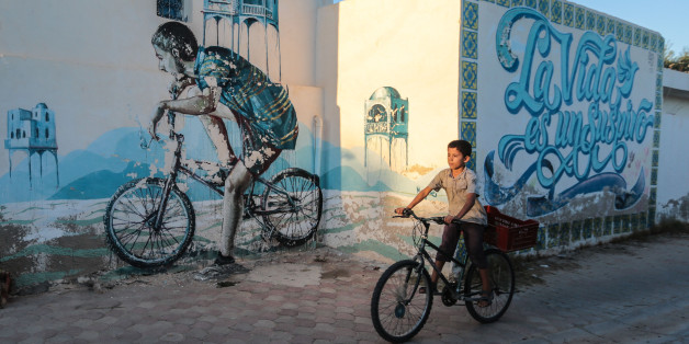 A Tunisian boy cycles past street art in Erriadh, a village on the resort island of Djerba, south of Tunis, Tunisia, Wednesday, Oct. 28, 2015. (AP Photo/Mosa'ab Elshamy)