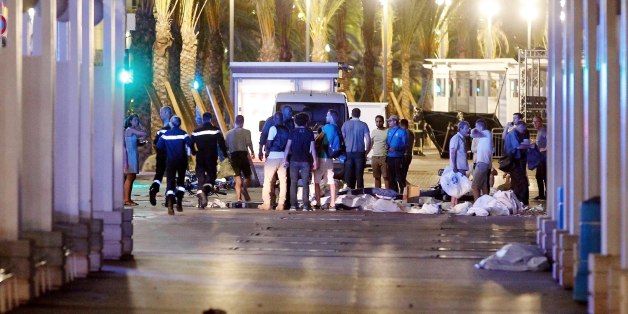 People stand next to covered bodies in the early hours of Friday, July 15, 2016, on the Promenade des Anglais in Nice, southern France. France has been stunned again as a large white truck killed many people after it mowed through a crowd of revelers gathered for a Bastille Day fireworks display late Thursday evening, in the Riviera city of Nice. (AP Photo)