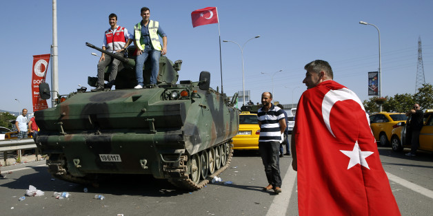 A man wrapped in a Turkish flag walks past a military vehicle in front of Sabiha Airport, in Istanbul, Turkey July 16, 2016. REUTERS/Baz Ratner