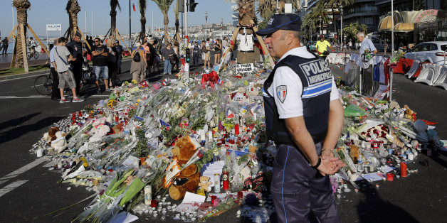 A police officer watches people gathering around a floral tribute for the victims killed during a deadly attack, on the famed Boulevard des Anglais in Nice, southern France, Sunday, July 17, 2016. French authorities detained two more people Sunday in the investigation into the Bastille Day truck attack on the Mediterranean city of Nice that killed at least 84 people, as authorities try to determine whether the slain attacker was a committed religious extremist or just a very angry man. (AP Photo/Laurent Cipriani)