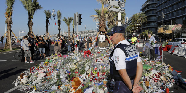 A police officer watches people gathering around a floral tribute for the victims killed during a deadly attack, on the famed Boulevard des Anglais in Nice, southern France, Sunday, July 17, 2016. French authorities detained two more people Sunday in the investigation into the Bastille Day truck attack on the Mediterranean city of Nice that killed at least 84 people, as authorities try to determine whether the slain attacker was a committed religious extremist or just a very angry man. (AP Photo/Laurent Cipriani)
