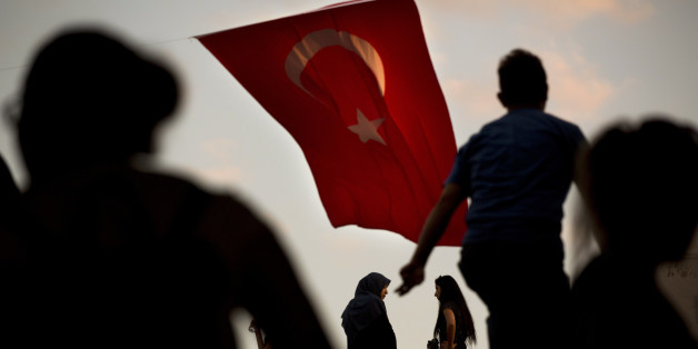 People walk by a Turkish flag in central Istanbul, Monday, July 18, 2016. Turkey's Interior Ministry has fired nearly 9,000 police officers, bureaucrats and others and detained thousands of suspected plotters following a foiled coup against the government, Turkey's state-run news agency reported Monday. (AP Photo/Emilio Morenatti)