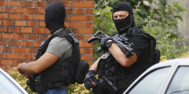 Police officers stand in front of a building during a search operation in Saint-Etienne-du-Rouvray, Normandy, France, following an attack on a church that left a priest dead, Tuesday, July 26, 2016. Two attackers invaded a church Tuesday during morning Mass near the Normandy city of Rouen, killing an 84-year-old priest by slitting his throat and taking hostages before being shot and killed by police, French officials said. (AP Photo/Francois Mori)