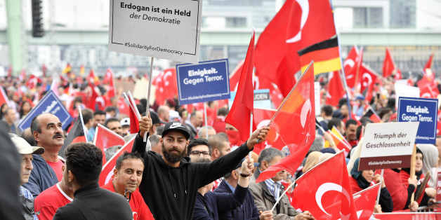 A Turkish protestor holds a banner reading 'Erdogan is a hero of democracy', left, during a demonstration in Cologne, Germany, Sunday, July 31, 2016. Supporters of Turkish President Recep Tayyip Erdogan demonstrate in Cologne amid heavy police presence. Some 30,000 participants are expected at Sunday's demonstration, which comes amid tensions following the failed coup attempt in Turkey and concern in Germany over the extent of the Turkish government's subsequent crackdown. (AP Photo/Martin Meissner)