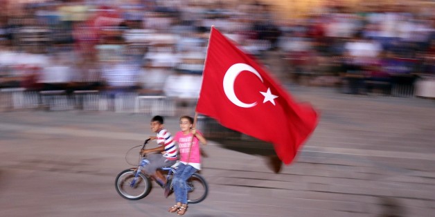 HATAY, TURKEY - JULY 30: Two Children wave Turkish flag as they ride on bicycle as people gather to protest against July 15 failed military coup attempt, at Iskenderun district of Hatay, Turkey on July 30, 2016. Turkish officials accuse U.S.-based Turkish citizen Fetullah Gulen plotting to overthrow the government of President Erdogan as the culmination of a long running campaign to infiltrate Turkish institutions including the military, the police and the judiciary. (Photo by Burak Milli/Anadolu Agency/Getty Images)