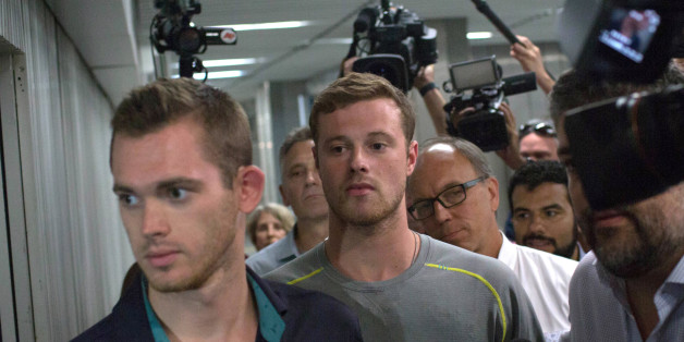 Journalists surround American Olympic swimmers Gunnar Bentz, left, and Jack Conger, center, as they leave the police station at Rio International airport early Thursday Aug. 18, 2016. The two were taken off their flight from Brazil to the U.S. on Wednesday by local authorities amid an investigation into a reported robbery targeting Ryan Lochte and his teammates. According to their lawyer they will not be allowed to leave Brazil until they provide testimony about the robbery. (AP Photo/Mauro Pime