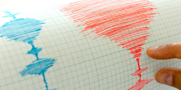 Seismological device for measuring earthquakes. Seismological activity live on the sheet of measuring paper. Earthquake wave on graph paper. Human hand showing earthquake.