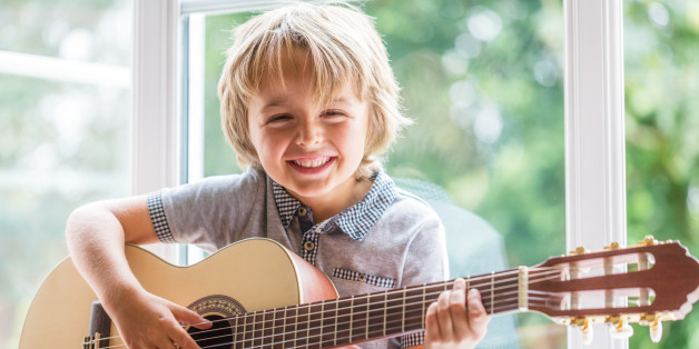 Happy smiling boy learning to play the acoustic guitar