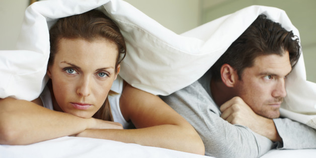 Portrait of an angry woman and her frustrated boyfriend lying beneath the bed covers