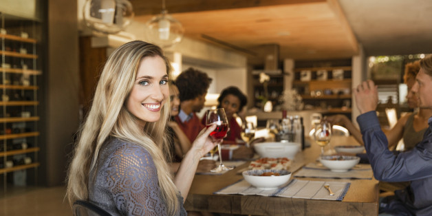 Smiling woman holding a glass at a table having dinner with friends.