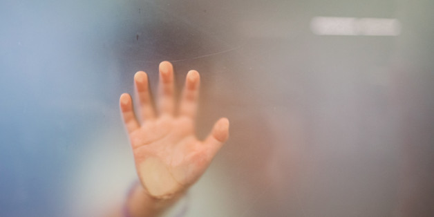 close up of the hand of a little girl putting her hand against a depolished glass from behind