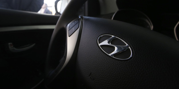 Employees talk next to Hyundai Motor's i30 car, with its logo seen on the steering wheel, at a Hyundai dealership in Seoul October 23, 2014. Hyundai Motor Co posted a 29 percent year-on-year fall in its quarterly net profit, missing analysts' estimates, hit by a strong local currency and slowing sales growth in its key U.S. and South Korean markets. REUTERS/Kim Hong-Ji (SOUTH KOREA - Tags: BUSINESS TRANSPORT LOGO)