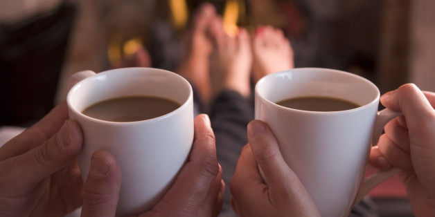 Feet warming at fireplace with hands holding coffee