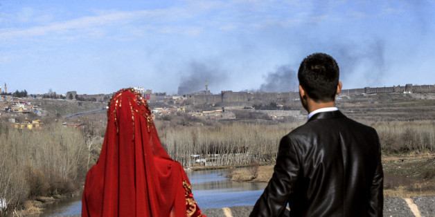 TOPSHOT - A couple hold hands for a wedding photo as they look at smokes rising over the district of Sur in Diyarbakir on February 3, 2016 after clashes between Kurdish rebels and Turkish forces.
Four Turkish soldiers were killed on January 27, 2016 in clashes with Kurdistan Worker's Party (PKK) militants in Diyarbakir in southeast Turkey, as a controversial curfew order was expanded to new areas in the Kurdish-dominated city. / AFP / ILYAS AKENGIN (Photo credit should read ILYAS AKENGIN/AFP/Getty Images)