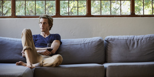 Mid adult man holding red wineglass while sitting on sofa at home