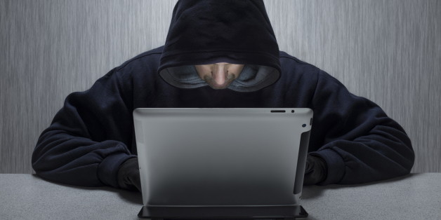 An anonymous hooded male using a tablet computer to represent a cyber criminal. (Photo by: Loop Images/UIG via Getty Images)