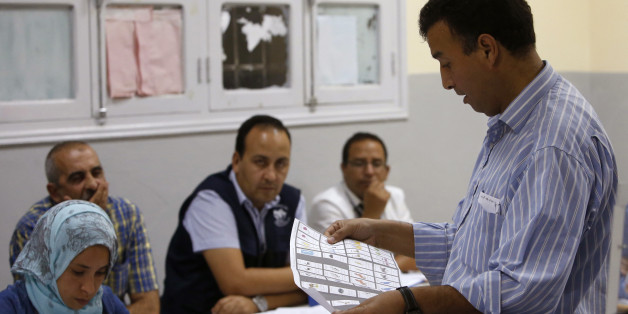 The president of a polling station checks a ballot as officials and political party's representatives count the ballots as from left to right observers Moroccan Omar Eloufir from Moroccan League for Citizenship and Law Man, Tunisian Mouldi Ayari from Election Network in the Arab Region and Moroccan Ahmed Bazzi from National Observatory of voter rights second right , back, look on in the polling station in Rabat, Morocco, Friday, Oct. 7, 2016. Amid worries about jobs and extremism, millions of Moroccans voted Friday in parliamentary elections that will determine whether moderate Islamists will keep control of the government or lose power to a young rival party close to the powerful royal palace. (AP Photo/Abdeljalil Bounhar)