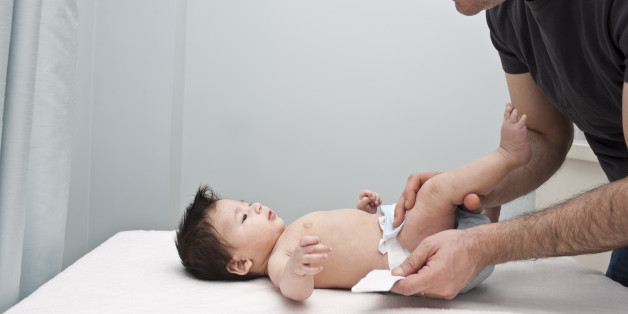 Happy, nurturing and smiling father changing his newborn son's diapers on a table. Image shows modern day fathers being more hands on and taking part in the day to day family activities with children and households