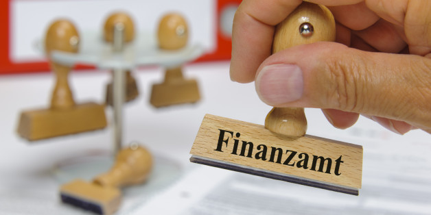 rubber stamp in hand marked with tax office, in german language - Finanzamt - over documents and tax forms
