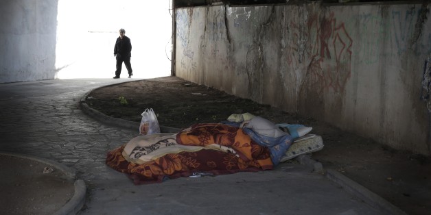 A homeless man sleeps under a bridge as an elderly woman walks past in Athens, Thursday March 19, 2015. Parliament on Wednesday approve an anti-poverty bill, that would provide assistance worth some 200 million euros ($212.7 million) to mostly jobless households considered to be in "extreme poverty." (AP Photo/Petros Giannakouris)