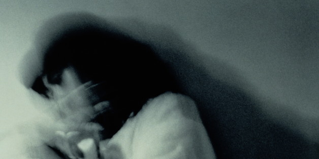 Woman curled on floor shielding herself with hands, blurred (B&W)
